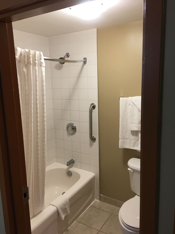 Un baño con bañera, cortina de ducha, barra de apoyo y un inodoro.
