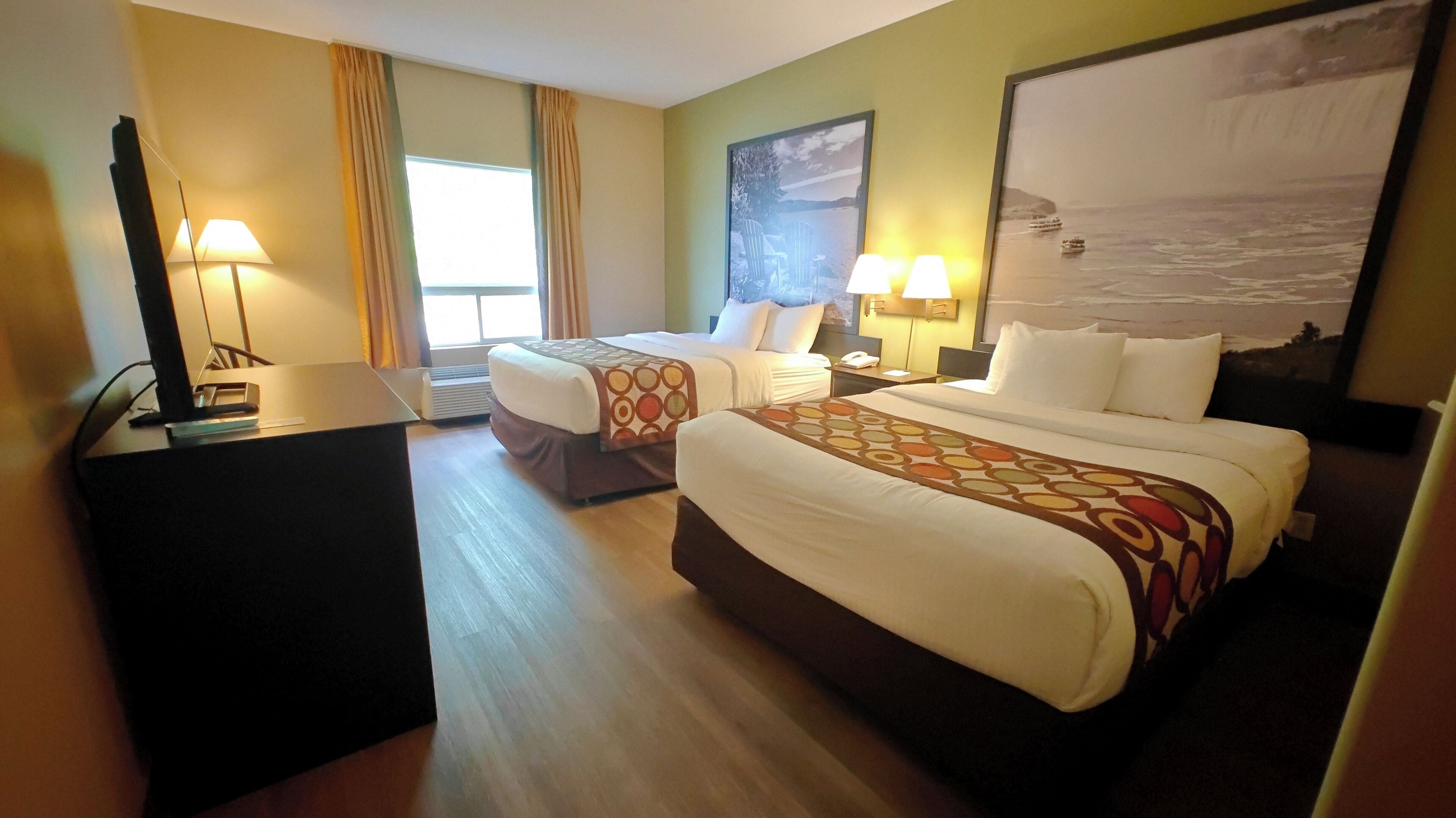 A hotel room with two beds, a desk, and a large window.