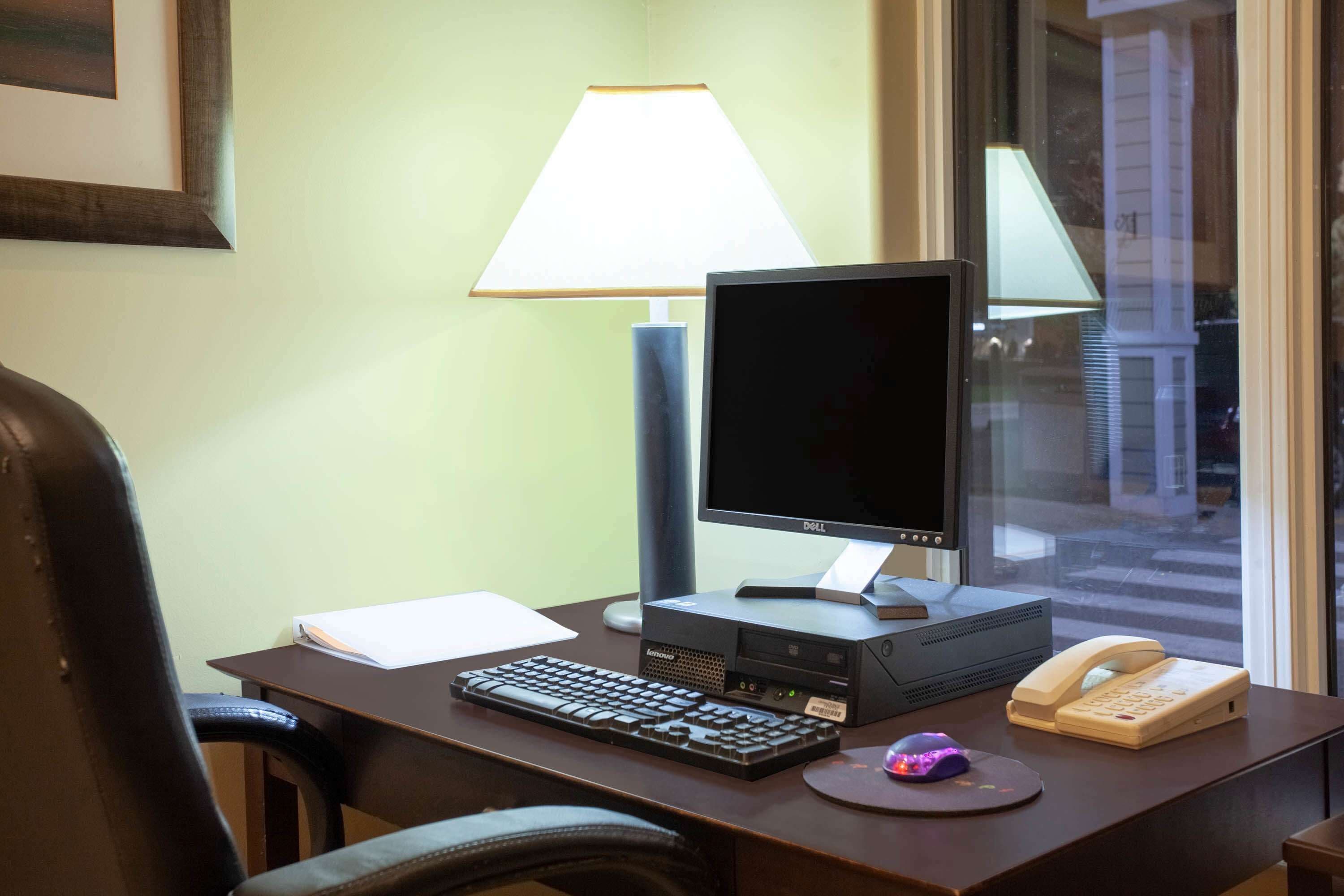 Mesa de quarto de hotel com computador, teclado, lâmpada, telefone e rato.