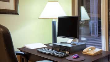 A hotel room desk with a computer, keyboard, lamp, telephone, and a mouse.