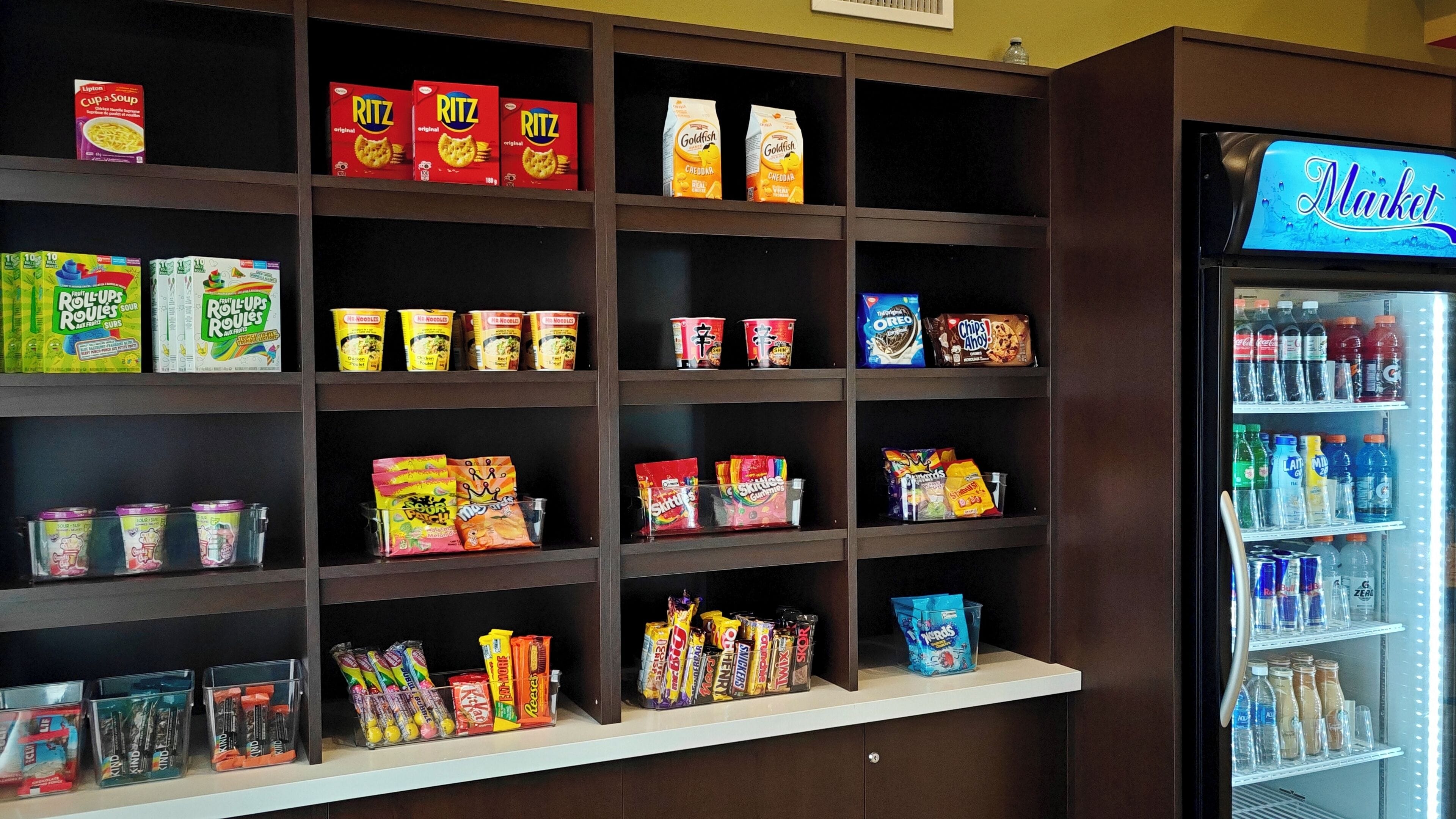 Esposizione di snack e bevande in un negozio, con prodotti assortiti come crackers Ritz, snack Goldfish e una selezione di bibite e succhi di frutta.