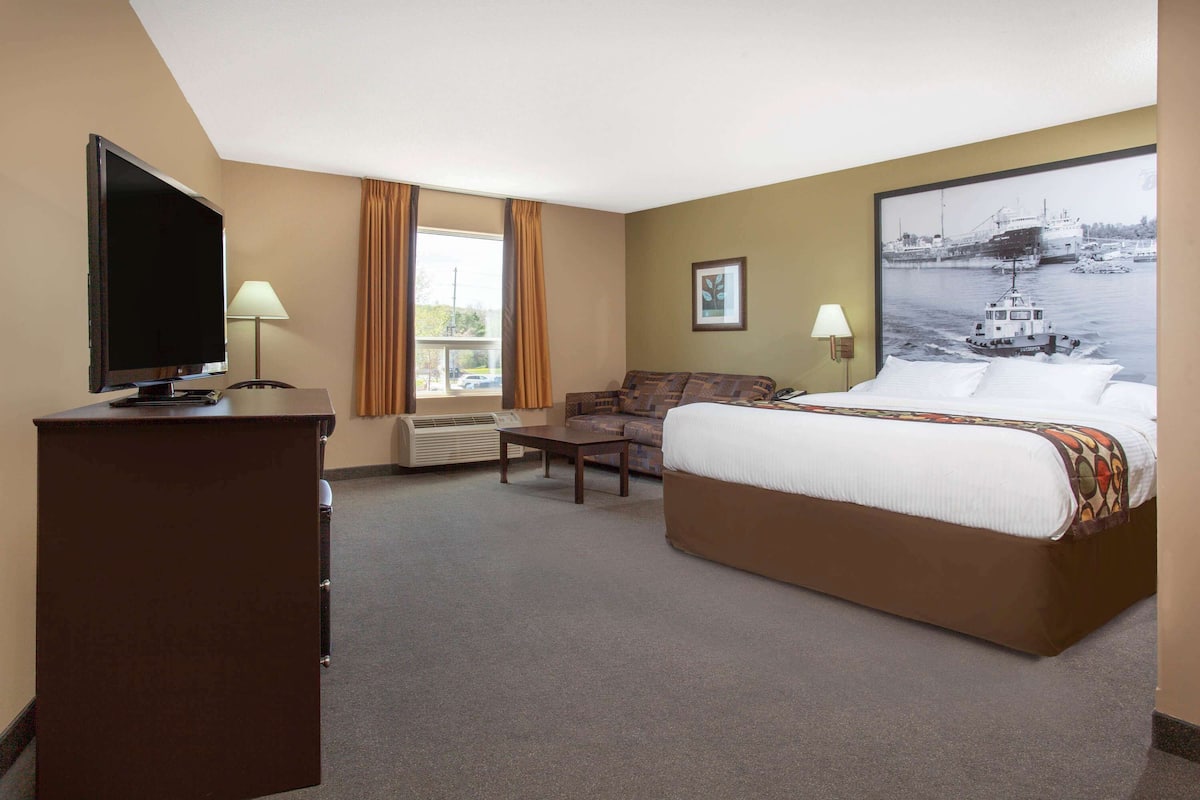 A hotel room with a bed, a desk, a chair, a television, and a large window with curtains.