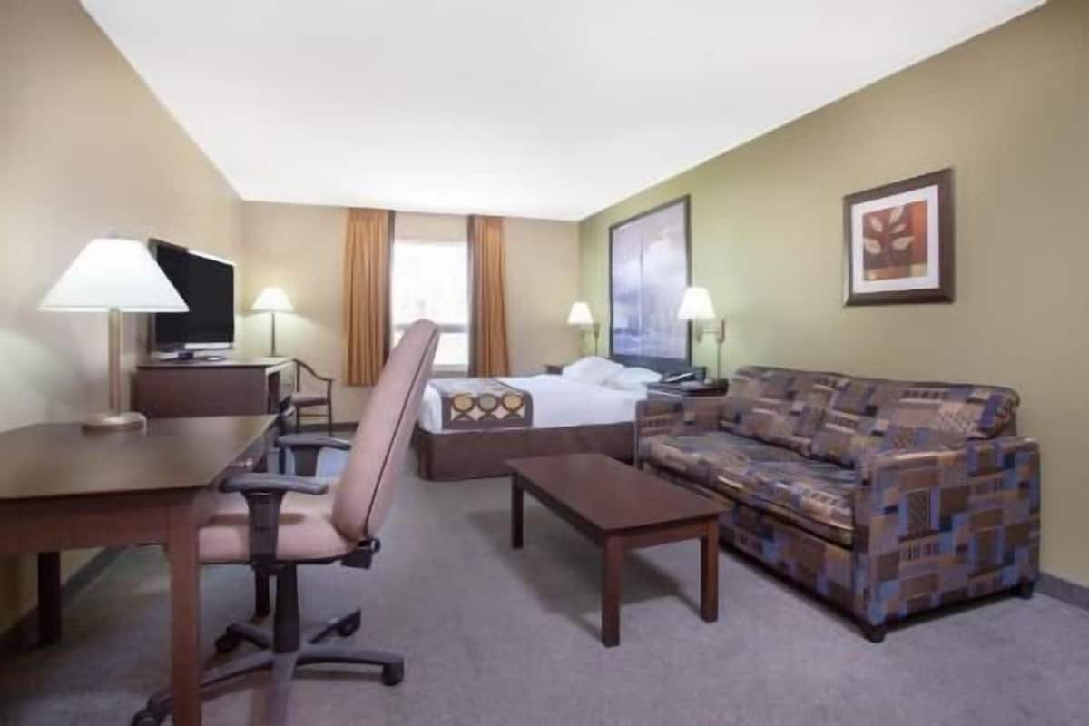 A hotel room with a bed, a sofa, a desk, a chair, and two lamps.