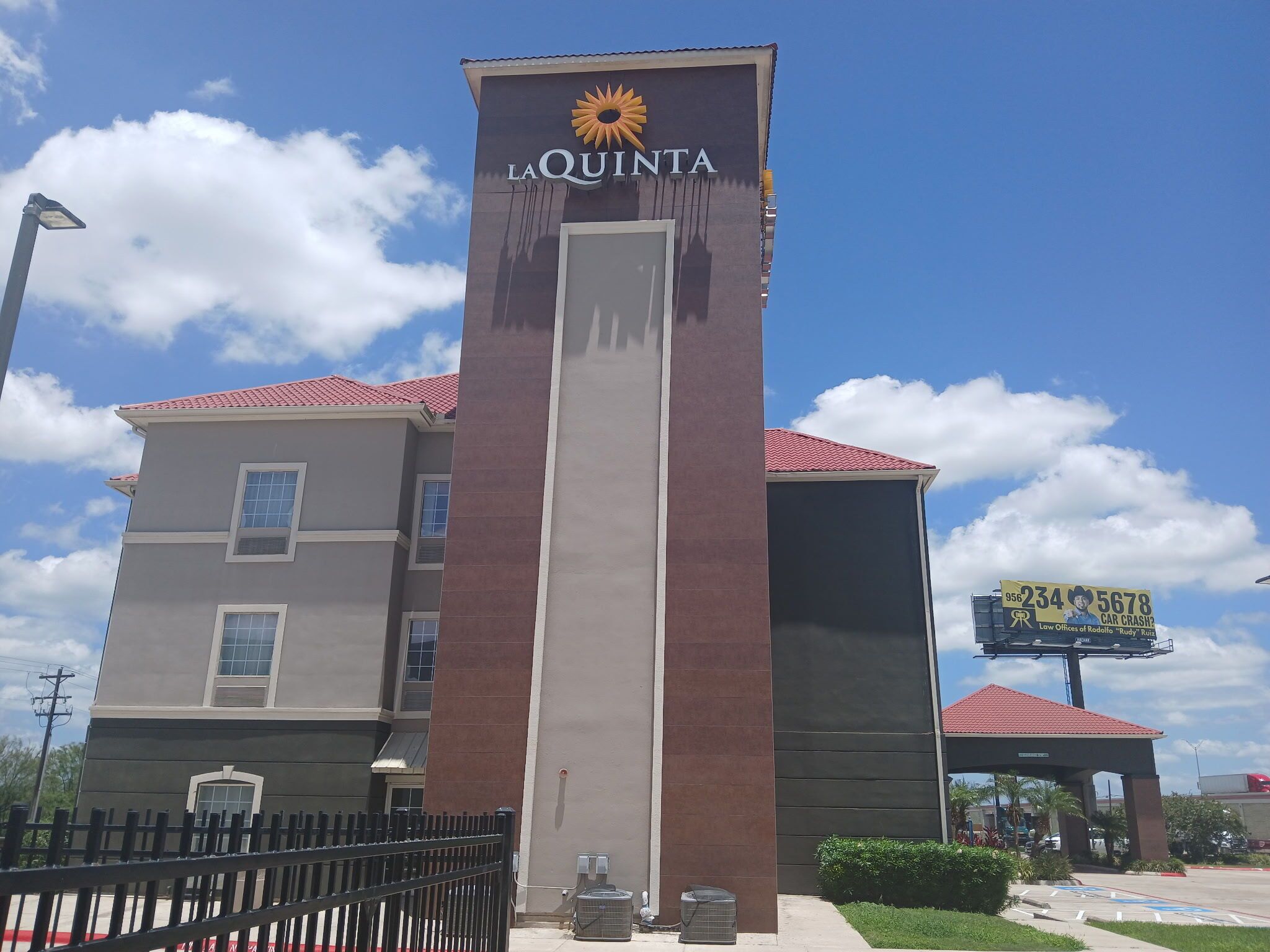 Un hotel con un cartel llamativo que dice 'LA QUINTA', techo de tejas rojas y un gran anuncio publicitario al fondo.