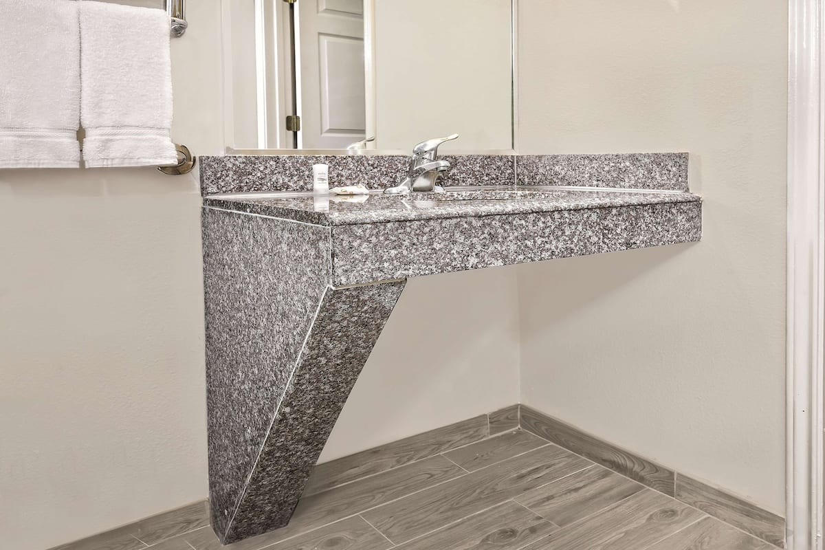 A bathroom with a granite countertop sink, a mirror, and a towel rack.