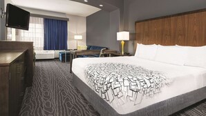 A hotel room with a large bed, a desk with a chair, a flat-screen TV mounted on the wall, and a window with blue curtains. - La Quinta Inn & Suites by Wyndham Mercedes Outlet Mall (Mercedes)