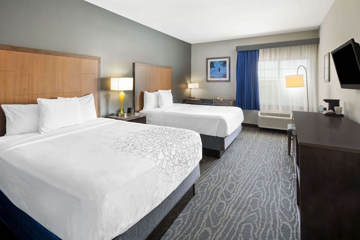 A hotel room with two beds, a desk, a TV, and a window with curtains.