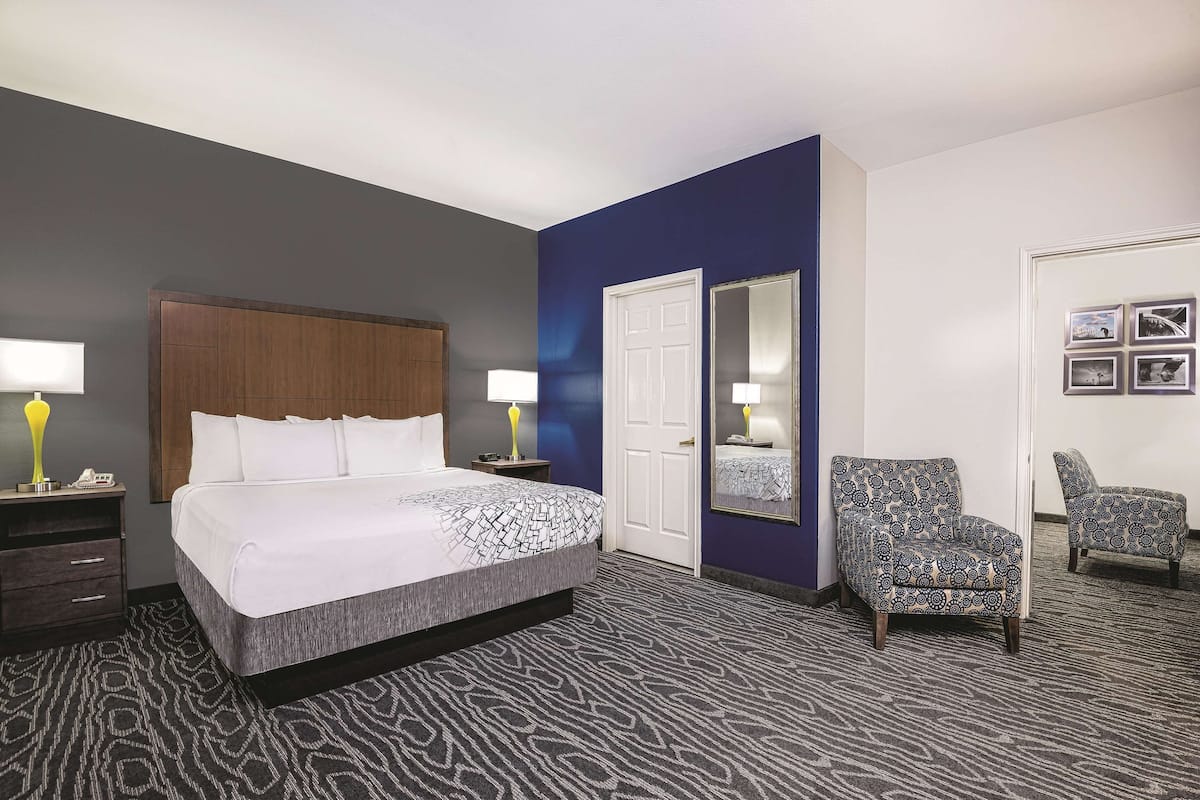 A hotel room with a large bed, two bedside tables with lamps, a chair, a mirror, and a door.