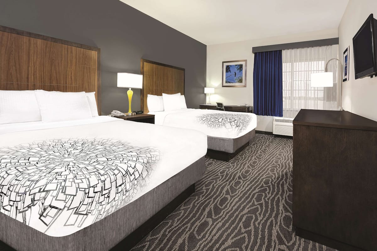 A hotel room with two beds, a desk, a chair, a lamp, a TV, and a window with curtains.
