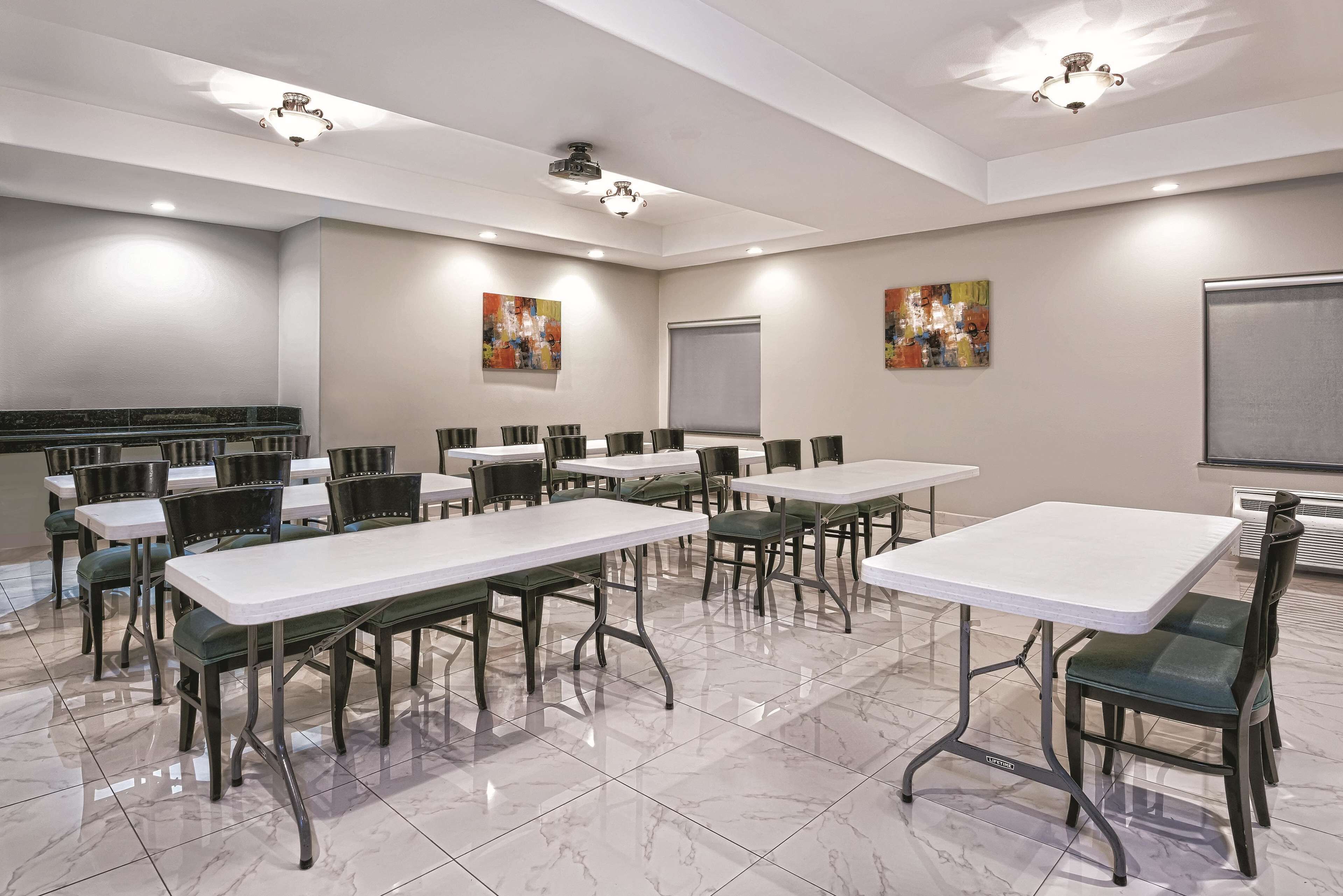 A conference room with multiple tables and chairs, ceiling lights, and artwork on the walls.