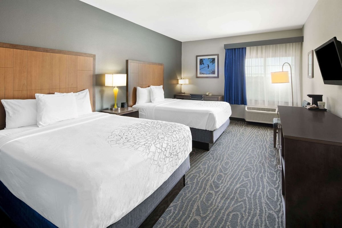 A hotel room with two beds, a desk, a TV, and a window with curtains.