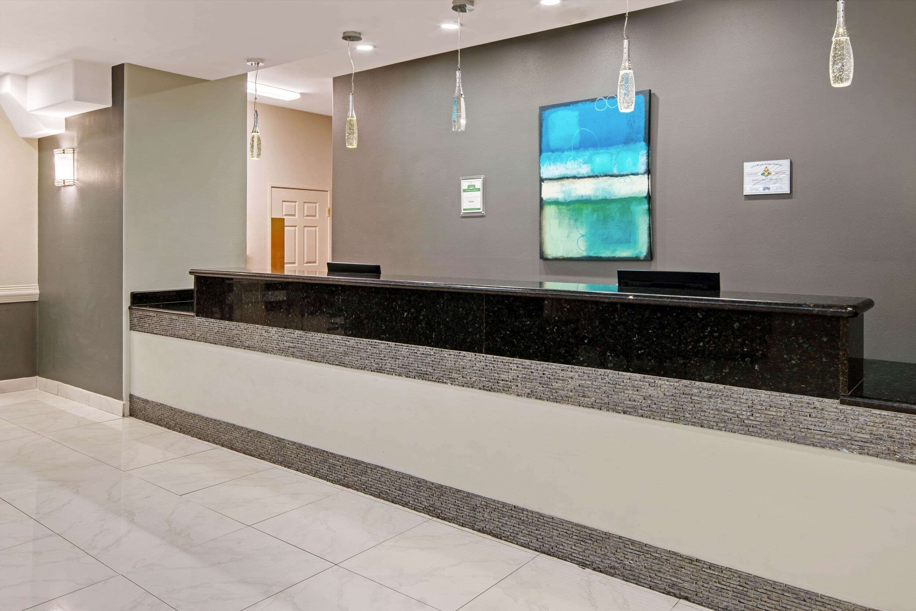 Un'area reception con un bancone in marmo, lampade a sospensione e un grande quadro astratto appeso al muro.