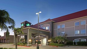 A hotel with a red roof and a green sign indicating it is a Marriott hotel. There are palm trees and a well-maintained lawn in front. - La Quinta Inn & Suites by Wyndham Mercedes Outlet Mall (Mercedes)