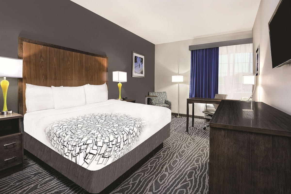 A hotel room with a large bed, a desk, a chair, and a television.