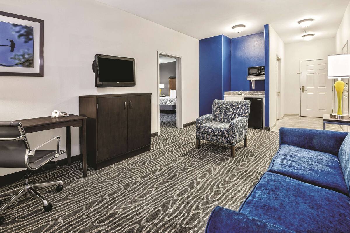 A hotel room with a desk, chair, sofa, and a TV mounted on the wall.