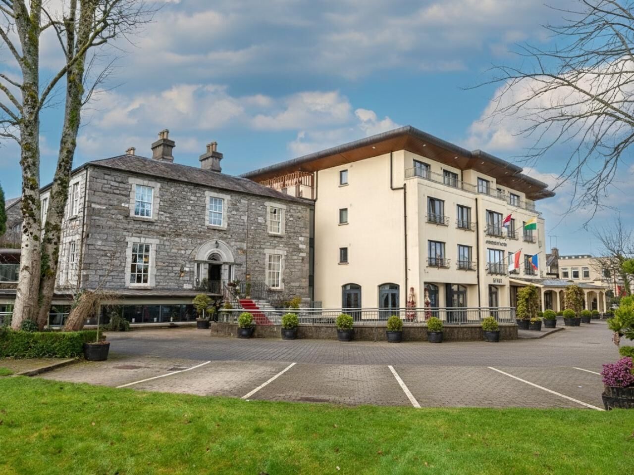Un hotel con fachada de piedra, una extensión moderna y un área de estacionamiento.