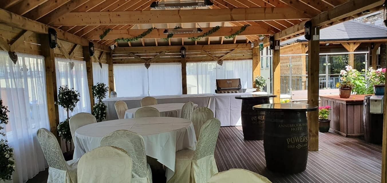 Um terraço coberto ao ar livre com mesas e cadeiras redondas, um espaço de bar e plantas em vasos.