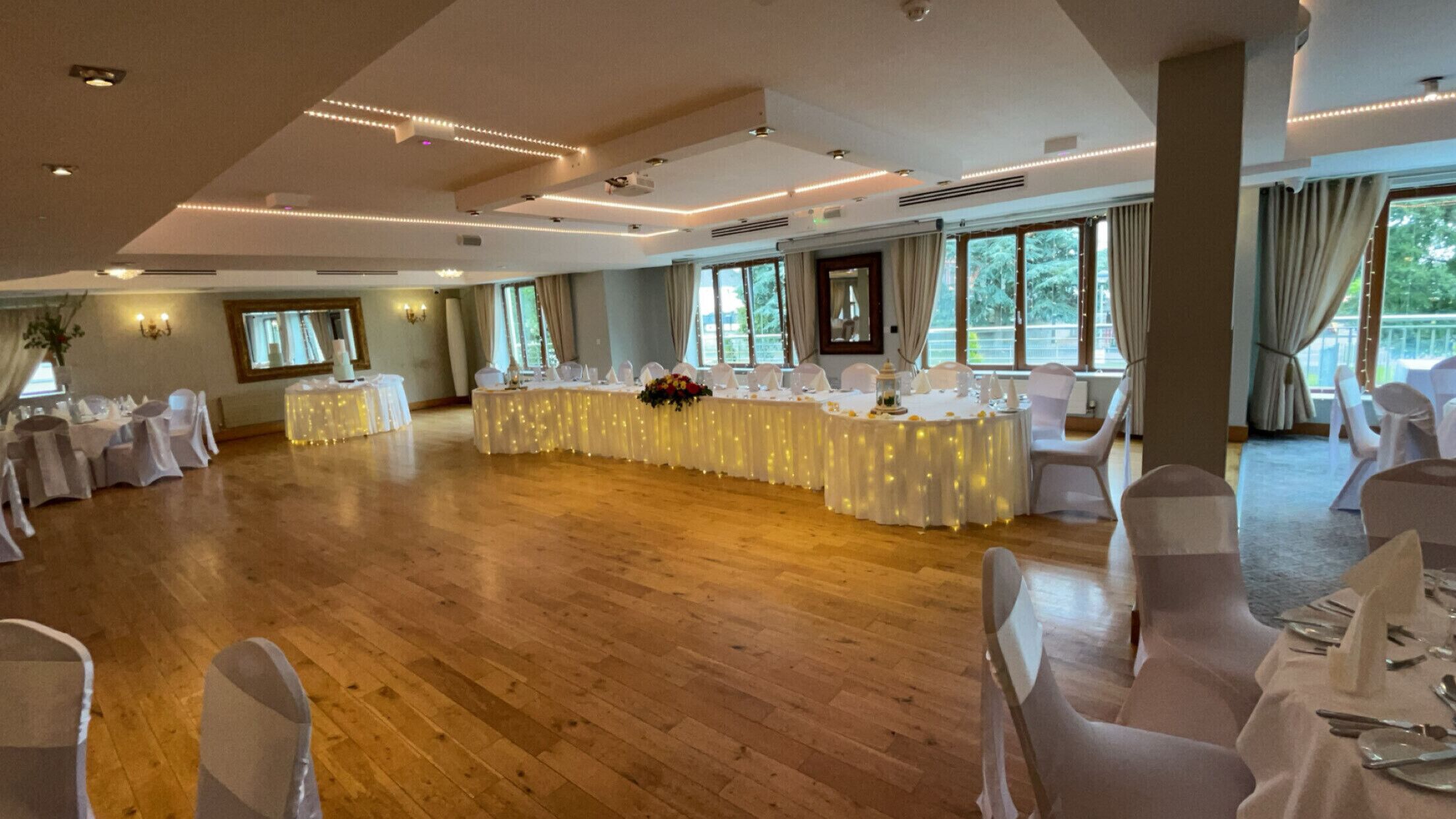 Een ruime zaal met ronde tafels, witte stoelen en grote ramen.