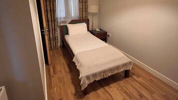 A bedroom with a single bed, a bedside table, a lamp, a ceiling light, and a window with curtains.