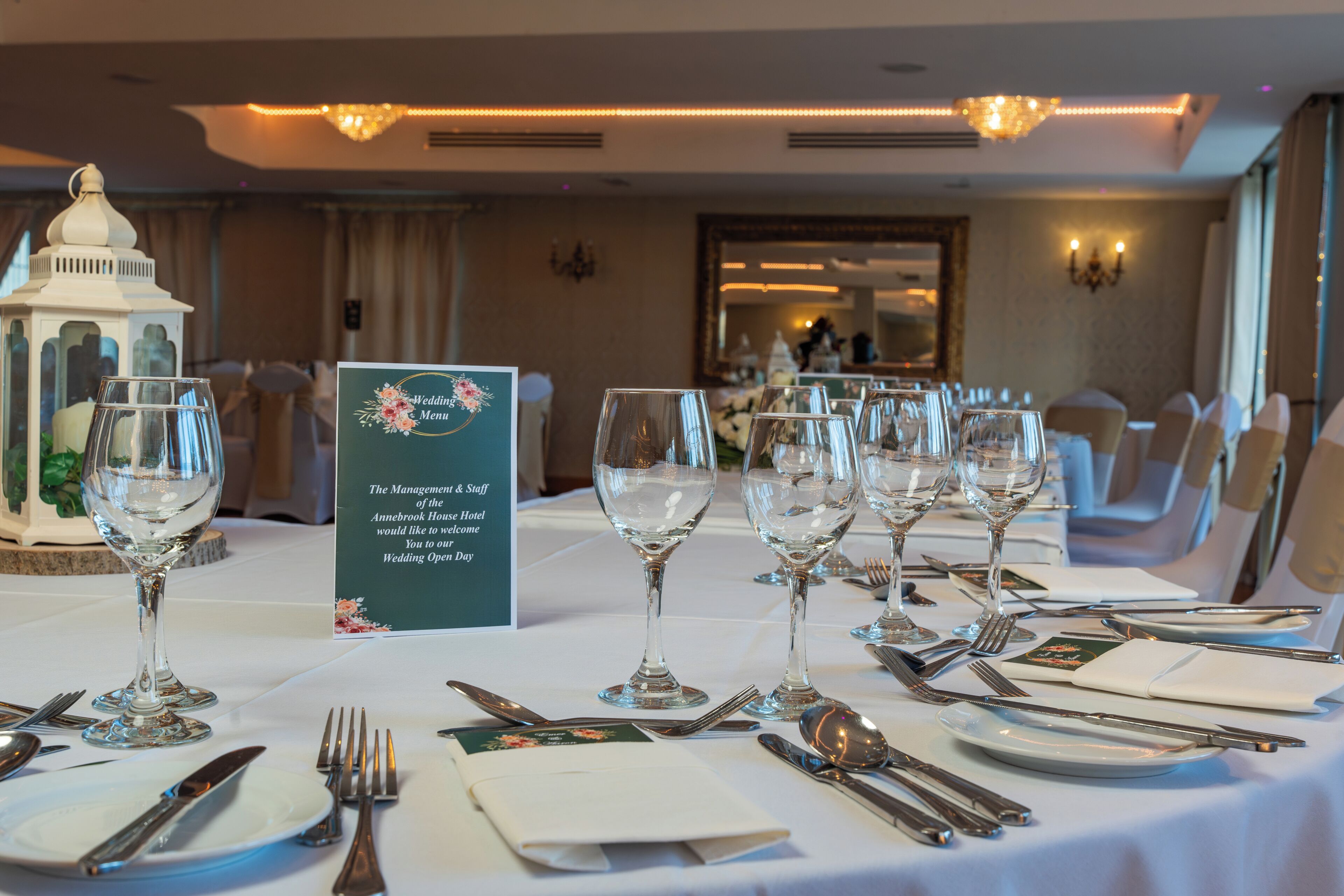 Une table dressée pour un banquet de mariage, avec une pancarte, des verres, des couverts et une lanterne.