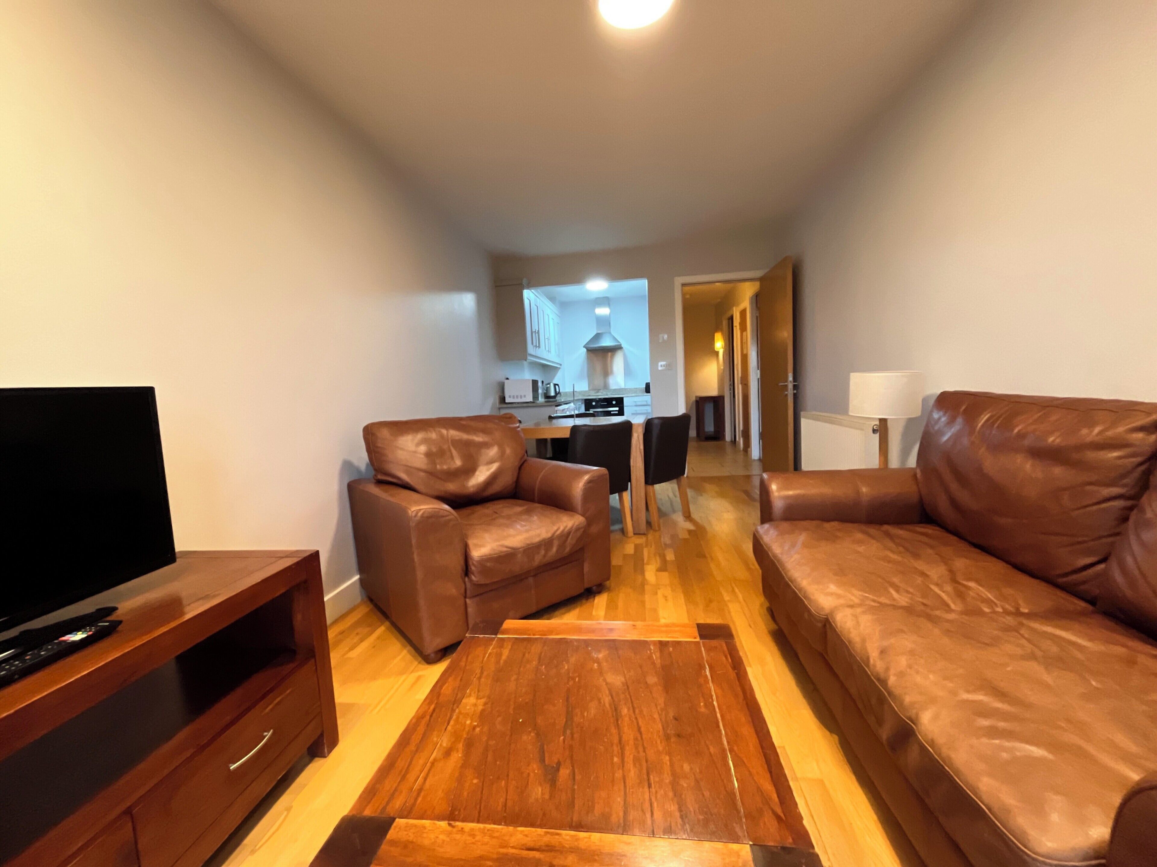 A living room with a sofa, a chair, a TV stand, and a wooden coffee table.