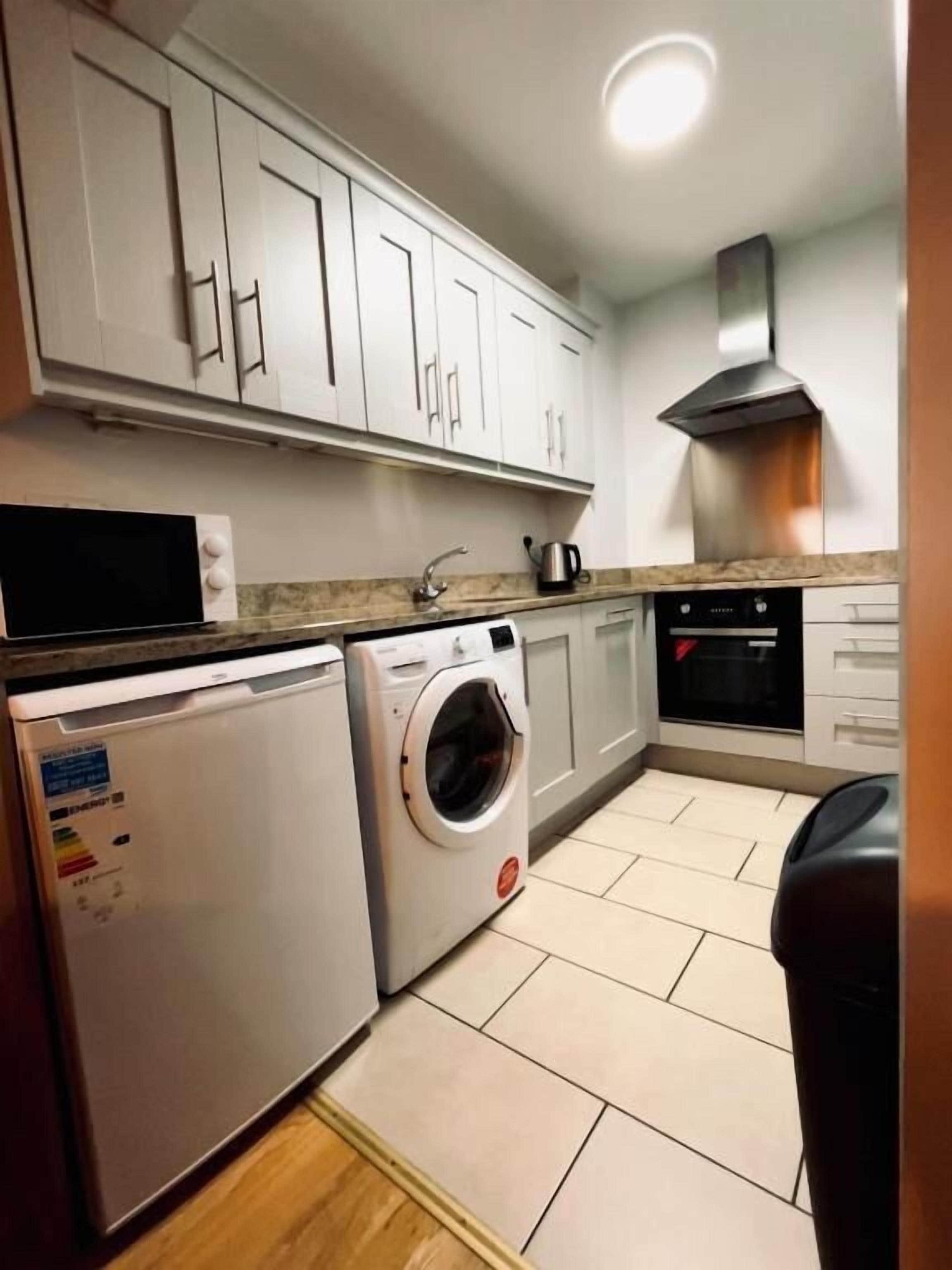 Una cocina compacta con armarios blancos, lavavajillas, lavadora y estufa.