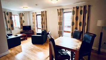 A living room with a wooden floor, a dining table with chairs, a sofa, a TV, and curtains with a polka dot pattern.