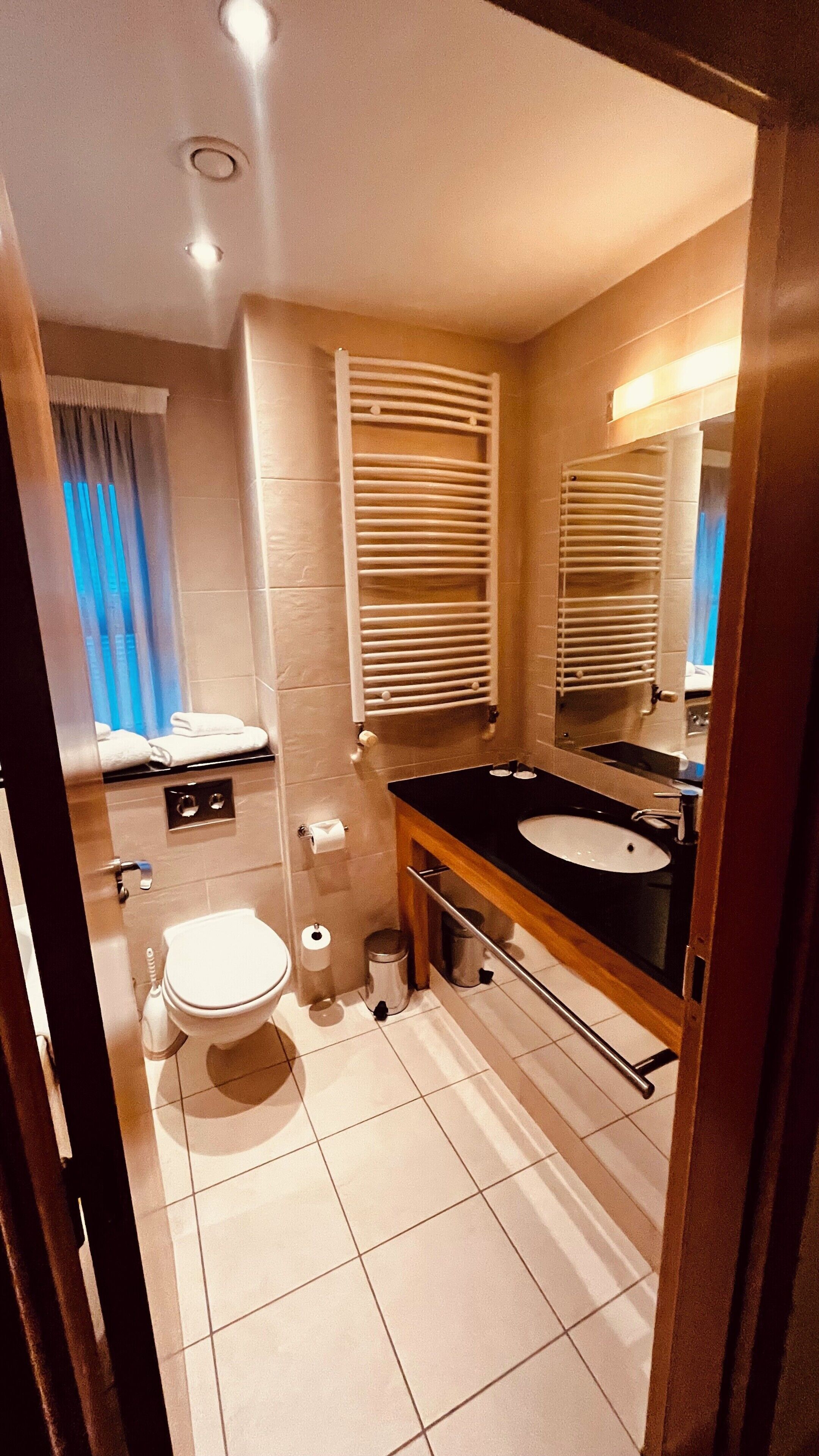 Un baño con inodoro, lavamanos, espejo, toallero y una ventana con persianas.