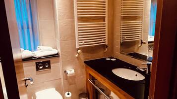 Un baño con inodoro, lavamanos, espejo, toallero y una ventana con persianas.