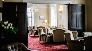 A room with a red carpet, multiple armchairs, a chandelier, and a large dark wooden door.