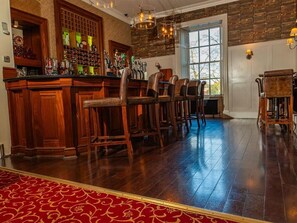A bar area with wooden bar counters, multiple stools, and a red patterned carpet. - Annebrook House Hotel (Mullingar)