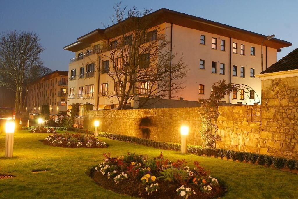 A multi-story building with a stone wall and a well-lit garden area.