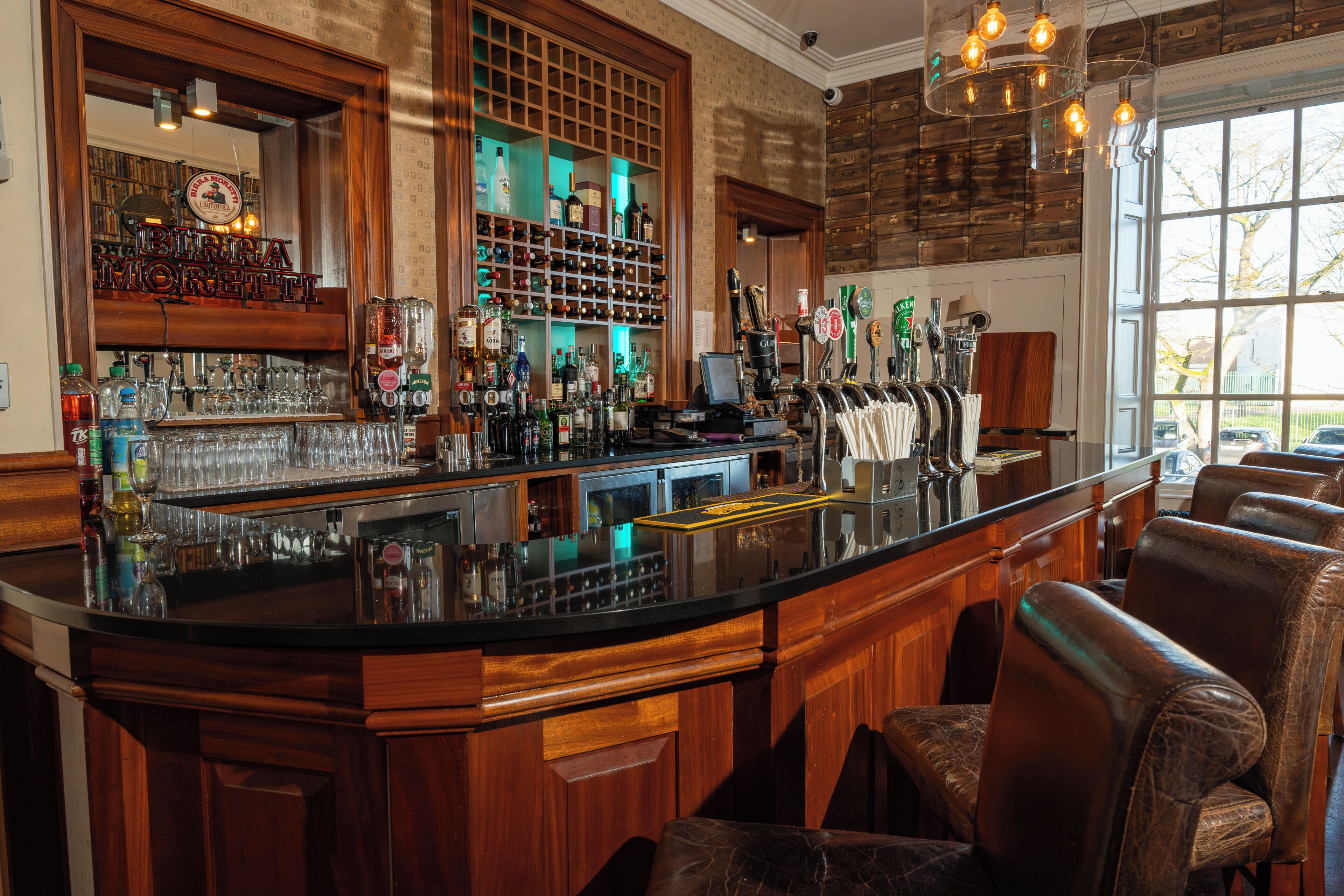 A bar area with a counter, bar stools, and a variety of bottles and glasses.