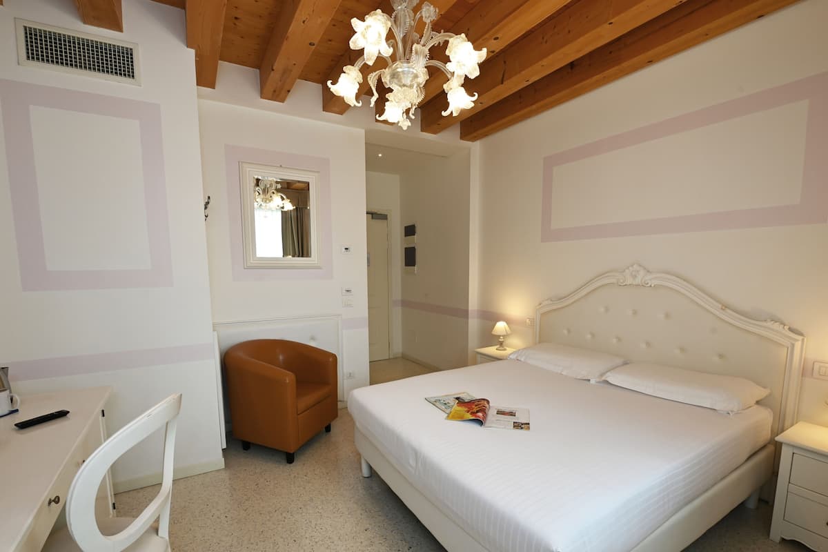 A bedroom with a bed, a desk, a chair, a nightstand, and a chandelier.