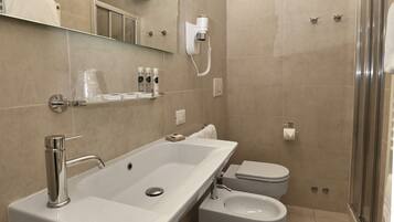 A modern bathroom with a large sink, toilet, bidet, and a glass-enclosed shower.