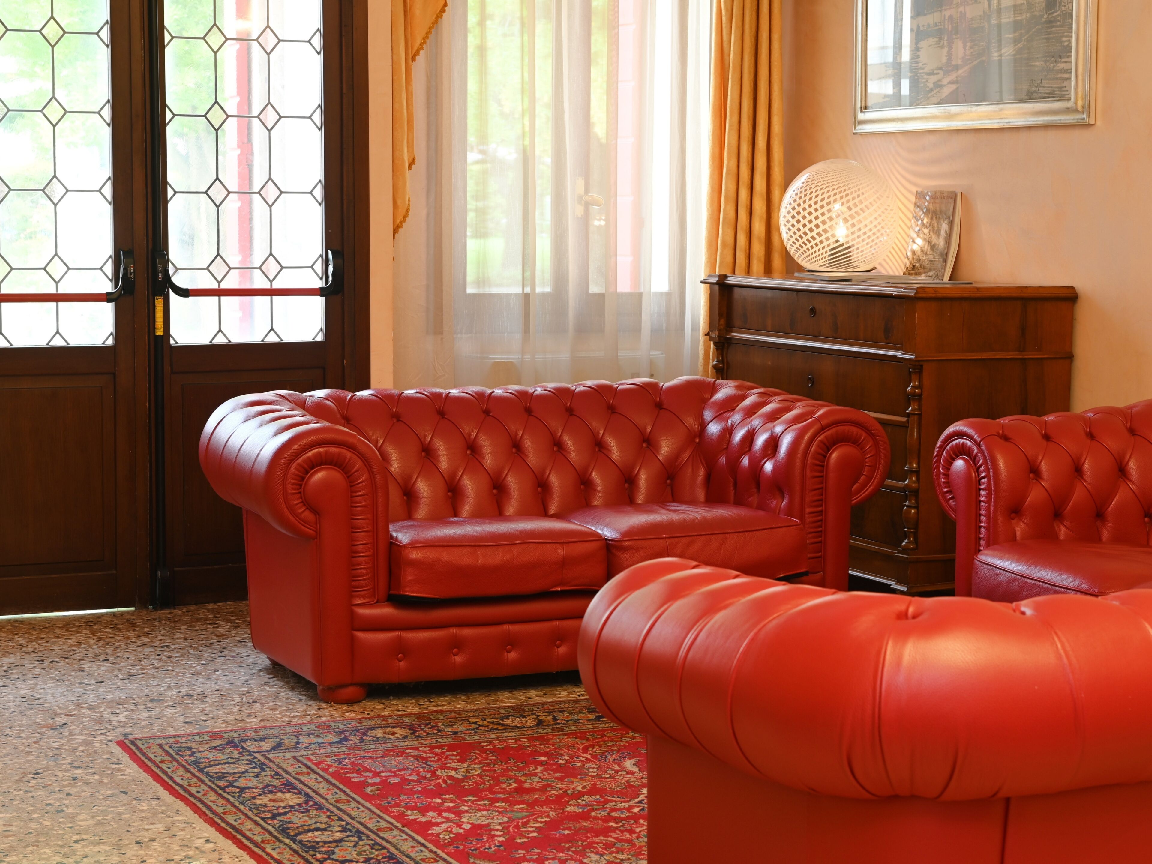 A room with a red leather sofa, a wooden cabinet, and a patterned rug.
