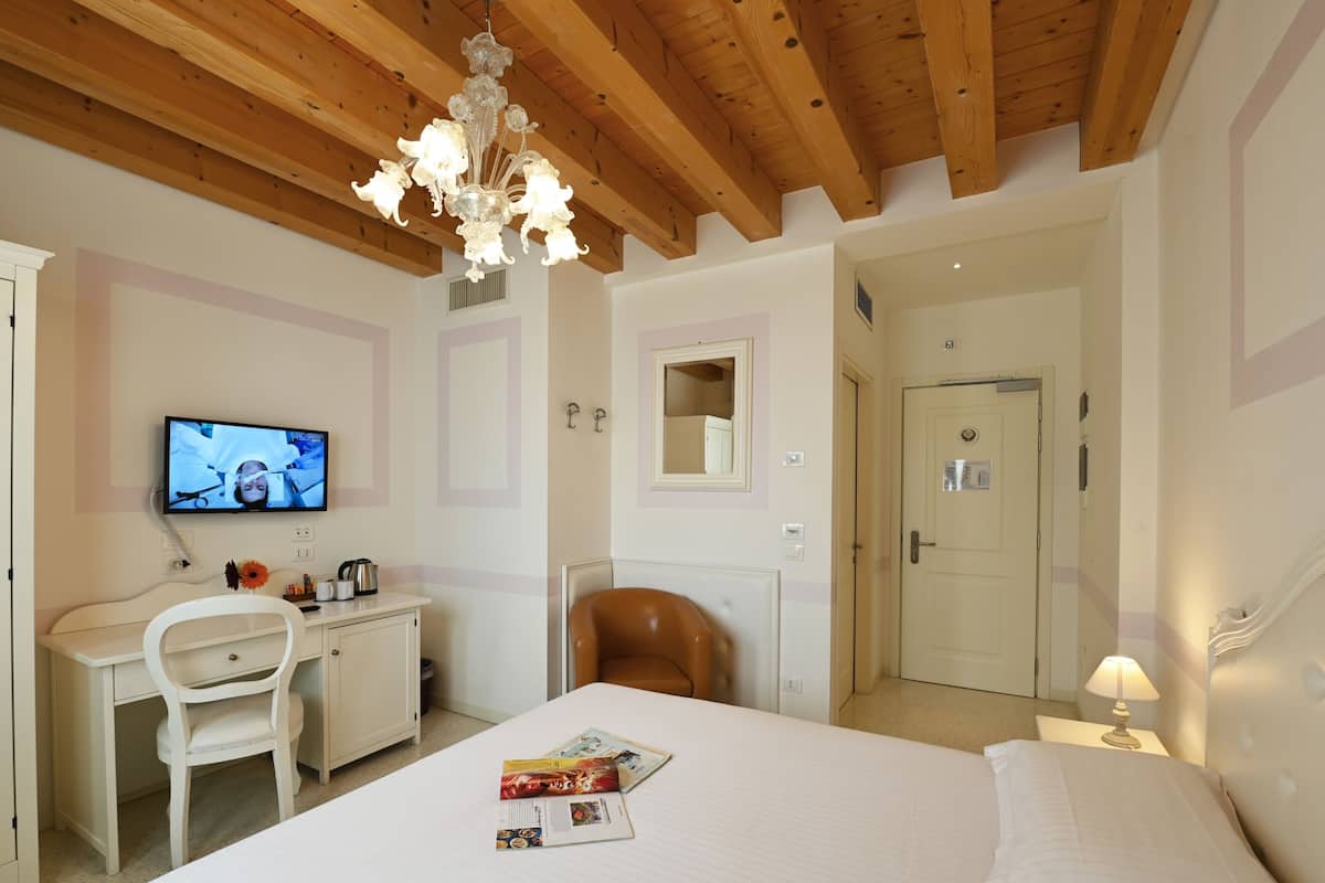 A bedroom with a bed, a desk, a chair, a television, and a door.