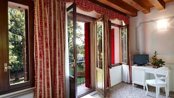 Ein Zimmer mit einem Bett, einem Schreibtisch mit Computer, einem Stuhl und einem Fenster mit Vorhängen.