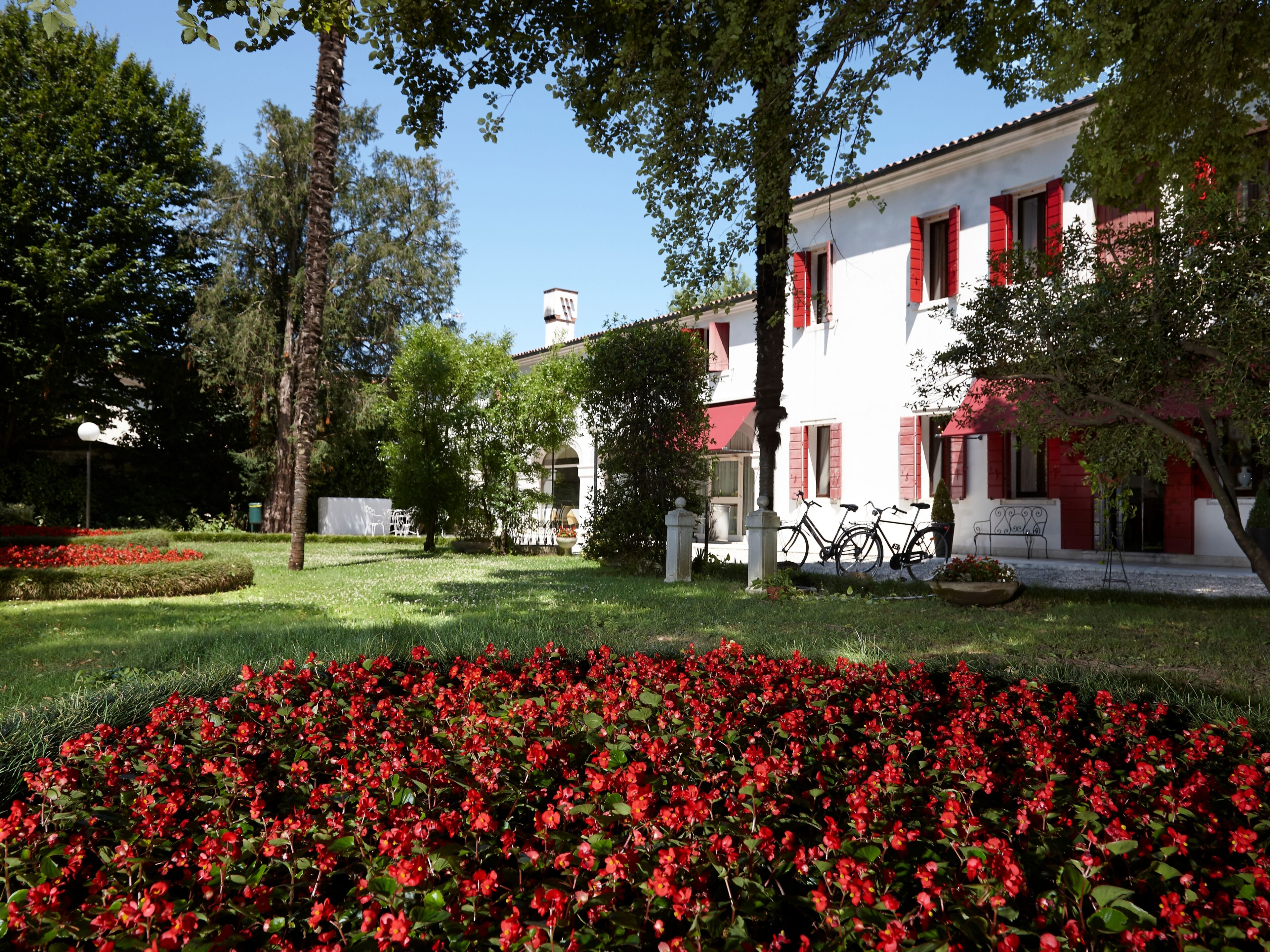 A building with red shutters, a garden with red flowers, and a clear sky.