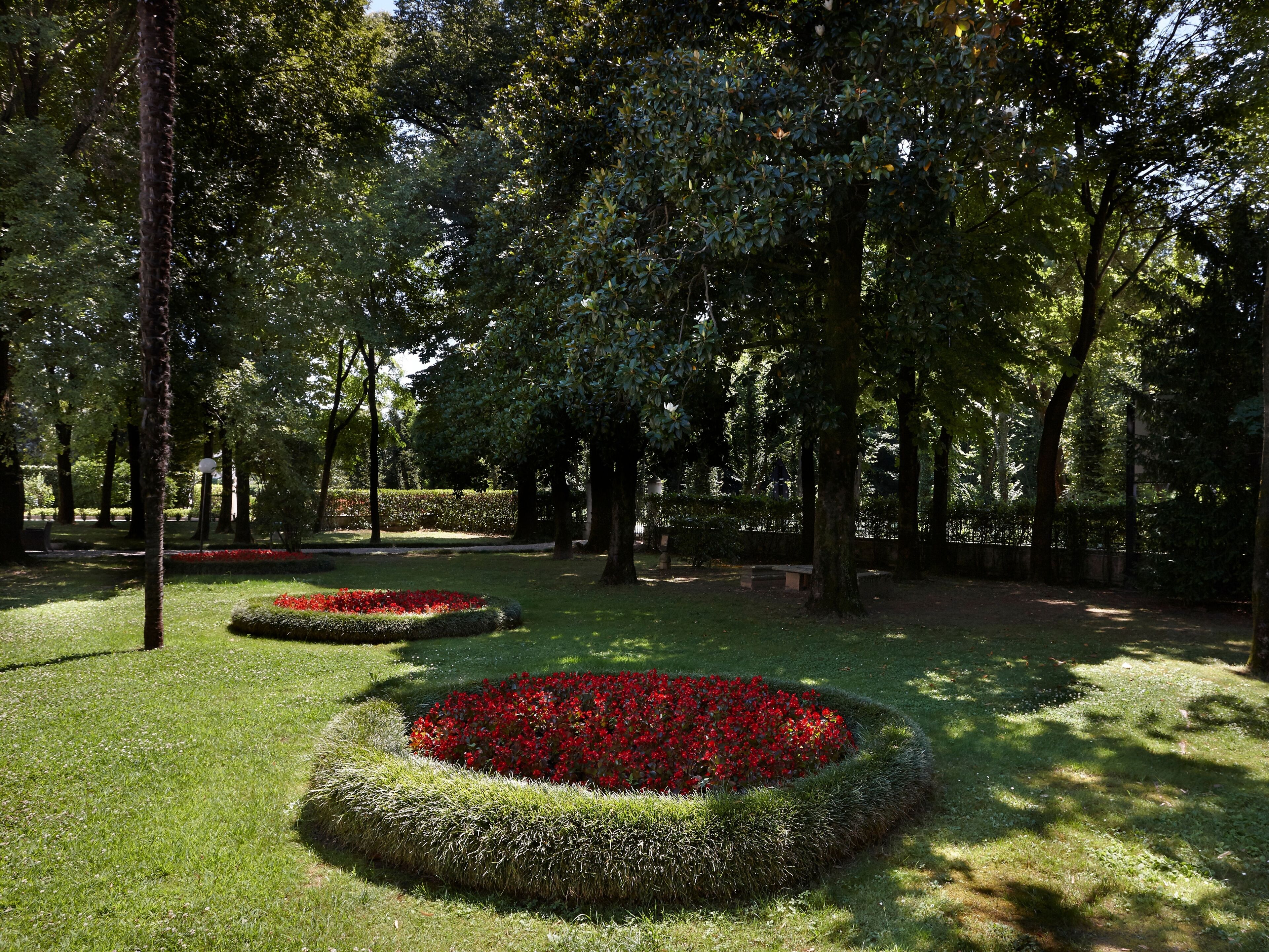Een park met ronde bloemperken en hoge bomen.