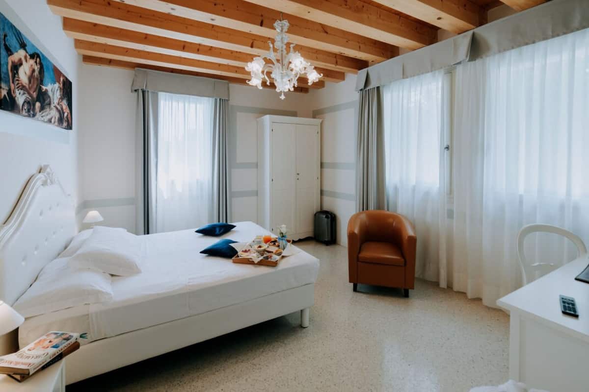 A hotel room with a bed, a desk, a chair, a chandelier, and a door.