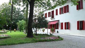 Un bâtiment aux volets rouges, une allée gravillonnée et un jardin bien entretenu agrémenté de fleurs roses.