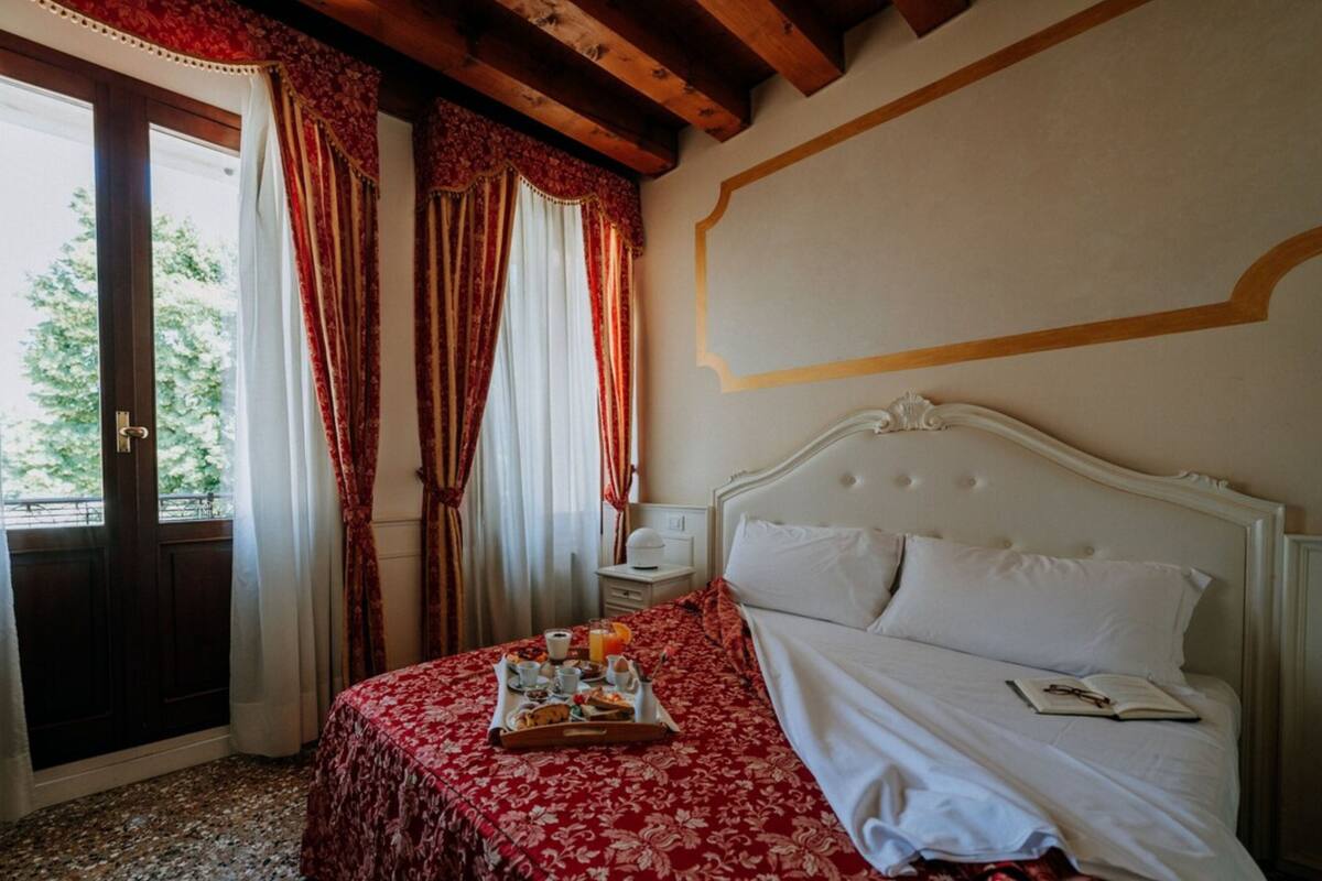 A hotel room with a bed, a tray of breakfast items, a nightstand, and a window with curtains.