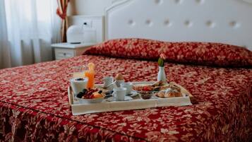 Un plateau de petit-déjeuner soigneusement préparé est posé sur un lit recouvert d’une courtepointe à motifs floraux rouges, avec une tête de lit blanche et un oreiller rouge.