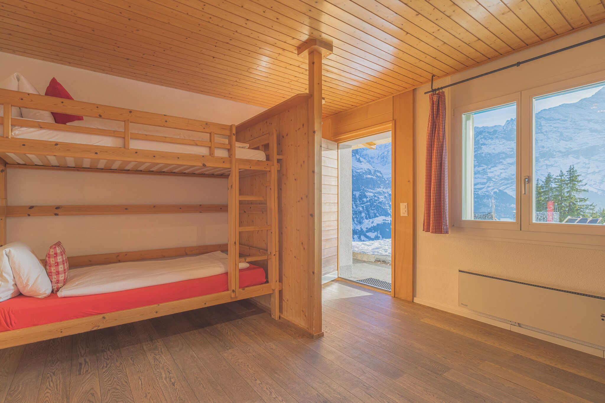 A wooden bunk bed room with a view of snow-covered mountains through a window.