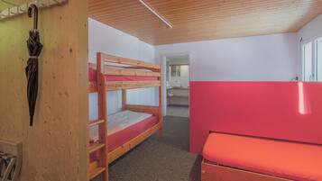 A bunk bed room with a red mattress, wooden ceiling, and a small bathroom visible through an open door.