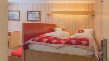A bedroom with a wooden bed, red and white bedding, and two framed pictures on the wall.