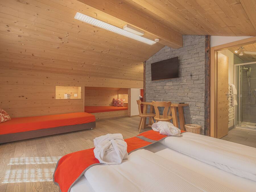 A modern hotel room with a wooden ceiling, a stone wall, a flat-screen TV, a shower, and a bed with a red blanket.