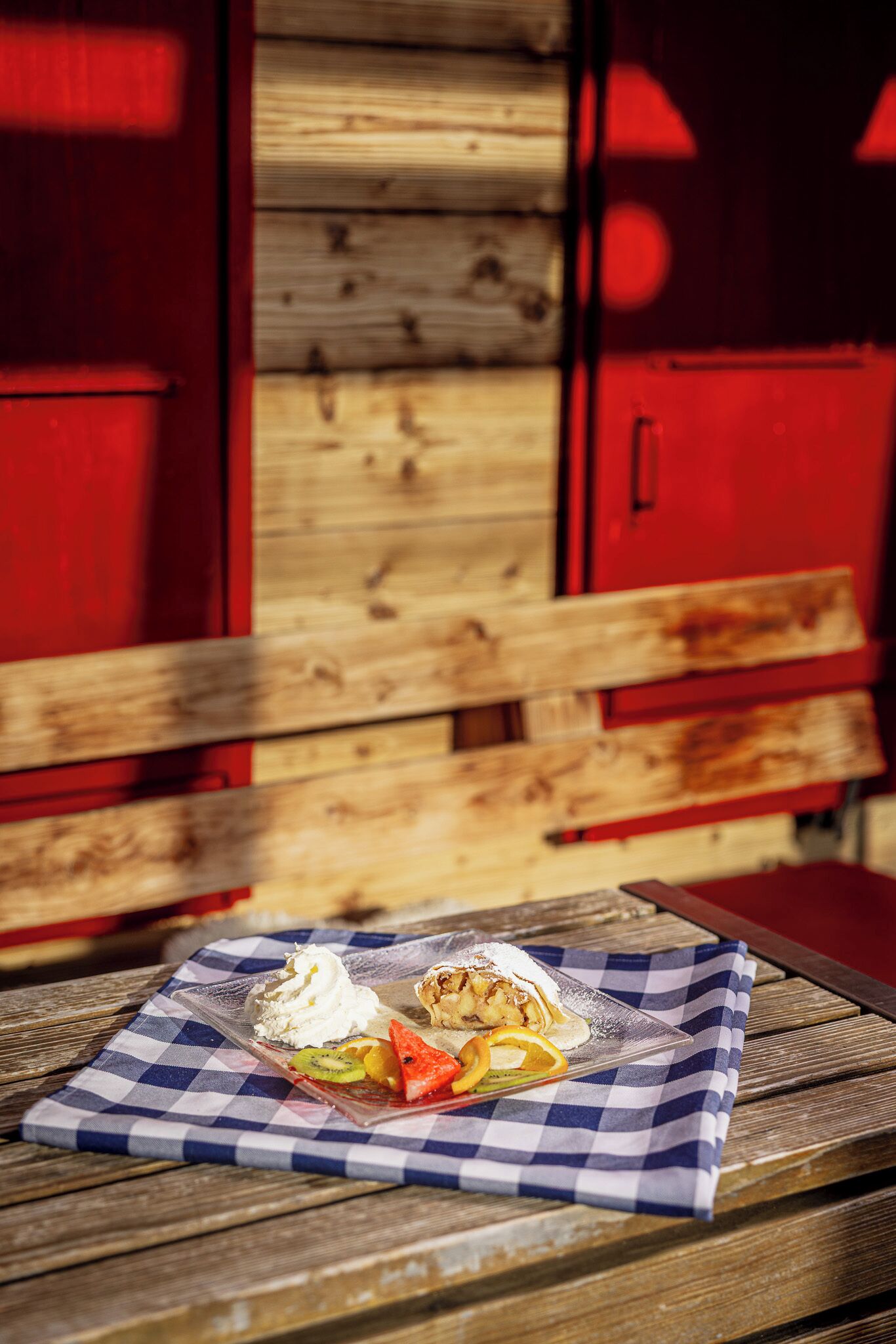 A dessert on a checkered cloth with fruits and whipped cream on a wooden table.