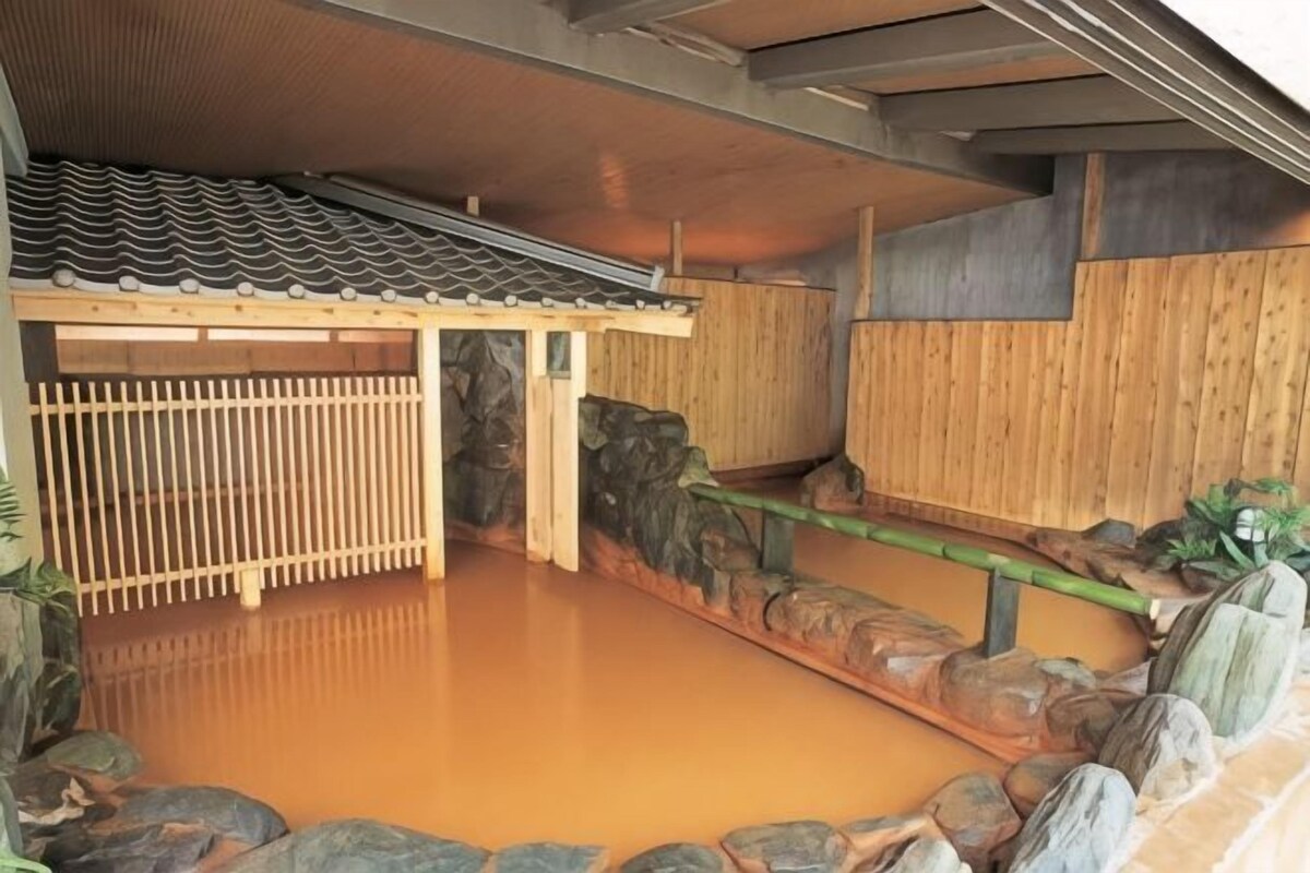 Un onsen japonés tradicional con un baño de madera, techo de tejas y pared de piedra.